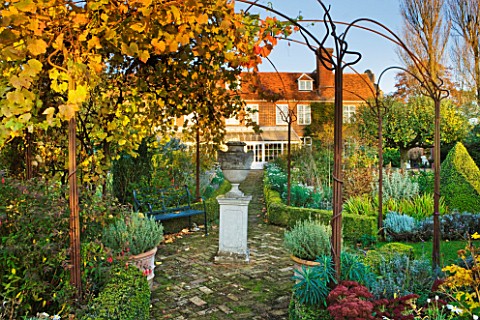 SALING_HALL__ESSEX__BRICK_PATH_LEADING_TO_HOUSE_AND_CONSERVATORY_WITH_URN_ON_PLINTH_AND_VINE_IN_AUTU