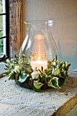 CANDLE IN GLASS JAR IN A WREATH WITH IVY  ROSES AND MISTLETOE IN WINDOWSILL : STYLING BY JACKY HOBBS