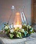 CANDLE IN GLASS JAR IN A WREATH WITH IVY  ROSES AND MISTLETOE IN WINDOWSILL : STYLING BY JACKY HOBBS
