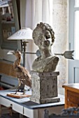 ROQUELIN  LOIRE VALLEY  FRANCE: DINING ROOM; STONE GARDEN BUST AND METAL WEATHER VANE DISPLAYED ON PAINTED WOODEN DESK