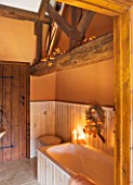 RICKYARD BARN HOUSE  OXFORDSHIRE: DESIGNERS JANE AND CLIVE NICHOLS. BATHROOM PAINTED WITH FIRED EARTH BRUSSELS ORANGE   EXPOSED BEAMS  BATH AND WREATH - CHRISTMAS