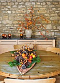 RICKYARD BARN HOUSE  OXFORDSHIRE: DESIGNERS JANE AND CLIVE NICHOLS. CHRISTMAS DECORATION ON TABLE - WICKER LEAF WITH FIR CONES  FRUIT AND BERRIES. CONTAINER WITH MALUS