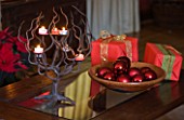 RICKYARD BARN HOUSE  OXFORDSHIRE: DESIGNERS JANE AND CLIVE NICHOLS. LIVING ROOM AT CHRISTMAS WITH WRAPPED PRESENTS  DARK RED BAUBLES IN A WOODEN BOWL AND CANDLE HOLDER