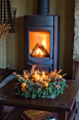 RICKYARD BARN HOUSE  OXFORDSHIRE: DESIGNERS JANE AND CLIVE NICHOLS. LIVING ROOM AT CHRISTMAS WITH CANDLE WREATH ON GLASS TOPPED COFFEE TABLE  WOOD BURNING FIRE