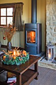 RICKYARD BARN HOUSE  OXFORDSHIRE: DESIGNERS JANE AND CLIVE NICHOLS. LIVING ROOM AT CHRISTMAS WITH CANDLE WREATH ON GLASS TOPPED COFFEE TABLE  WOOD BURNING FIRE