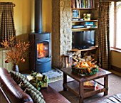 RICKYARD BARN HOUSE  OXFORDSHIRE: DESIGNERS JANE AND CLIVE NICHOLS. LIVING ROOM AT CHRISTMAS WITH CANDLE WREATH ON GLASS TOPPED COFFEE TABLE  LEATHER SOFAS  WOOD BURNING FIRE