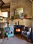 FULBROOK HOUSE: GALLERIED MAIN HALL WITH COTSWOLD STONE FIREPLACE  LOG BURNING STOVE AND LEATHER AND UPHOLSTERED ARMCHAIRS WITH CHRISTMAS TREE REFLECTED IN LARGE MIRROR.