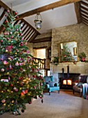 FULBROOK HOUSE: GALLERIED MAIN HALL WITH COTSWOLD STONE FIREPLACE  LOG BURNING STOVE  MIRROR AND LEATHER AND UPHOLSTERED ARMCHAIRS WITH CHRISTMAS TREE