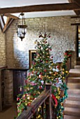 FULBROOK HOUSE: GALLERIED MAIN HALL WITH CEILING BEAMS  STONE WALLS  WOODEN STAIRCASE DECORATED TO MATCH CHRISTMAS TREE.