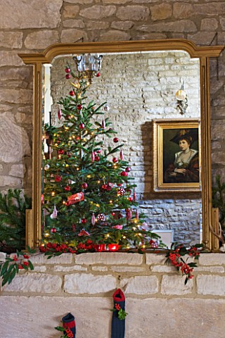FULBROOK_HOUSE_GALLERIED_MAIN_HALL_GILT_MIRROR_ABOVE_STONE_FIREPLACE_REFLECTING_CHRISTMAS_TREE