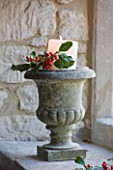 FULBROOK HOUSE: STONE PLANTER WITH CHURCH CANDLE AND HOLLY STANDS IN COTSWOLD STONE DEEP WINDOWSILL.