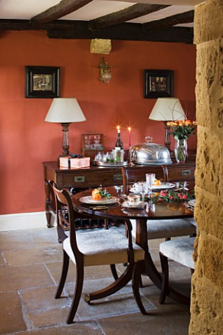 FULBROOK_HOUSE_DINING_ROOM_SET_FOR_ENTERTAINING_WITH_TERRACOTTA_PAINTED_WALL__BEAMED_CEILING_AND_STO