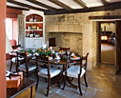 FULBROOK HOUSE: DINING ROOM SET FOR ENTERTAINING WITH TERRACOTTA PAINTED WALL  BEAMED CEILING AND STONE FLOOR. DOOR LEADS INTO HALLWAY WITH WOODBURNER
