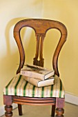 FULBROOK HOUSE: YELLOW DOUBLE BEDROOM - ANTIQUE POLISHED WOOD CHAIR WITH GOLD AND GREEN STRIPE FABRIC SEAT WITH OLD BOOKS