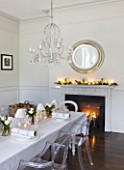 WHITE HOUSE: WHITE DINING ROOM WITH CENTRAL GLASS CHANDELIER AND SILVER ROUND MIRROR ABOVE MANTEL PIECE. LONG DINING TABLE DRESSED IN WHITE LINEN WITH TRANSPARENT GHOST CHAIRS