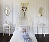 WHITE HOUSE: GIRLS BEDROOM WITH WHITE WALL PANELLING  OVAL WALL MIRRORS  CROWN STYLE LIGHT  SWEDISH STYLE IVORY PAINTED WOODEN BED WITH SHEER CANOPY   WHITE BED LINEN