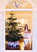 WHITE HOUSE: VIEW THROUGH DOUBLE FRENCH DOORS INTO LIVING ROOM - BOY AND GIRL ON SEAT WITH CHRISTMAS TREE AND PRESENTS