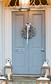WHITE HOUSE: HOUSE FRONT WITH PALE GREY FRONT DOOR DECORATED WITH WHITE GYPSOPHILA CHRISTMAS WREATH AND METAL LANTERNS