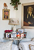 SARAH BAKERS HOUSE  THE OLD VICARAGE  SOMERSECORNER OF SITTING ROOM WITH FAMILY PHOTO COLLECTION   BAKER AND GRAY LAMP  PAINTINGS ON THE WALL WITH CHRISTMAS BOUQUET OF FRESH HOLLY.