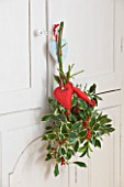SARAH BAKERS HOUSE  THE OLD VICARAGE: KITCHEN: SPRIGS OF VARIEGATED AND NON VAREIGATED HOLLY DECORATED WITH RED FELT HEARTS HANG FROM THE KITCHEN CUPBOARD.