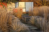 THE MANOR HOUSE  STEVINGTON  BEDFORDSHIRE. DESIGNER: KATHY BROWN - THE MONDRIAN BORDER IN FROST IN WINTER AT SUNSET WITH A WOODEN BENCH AND MONDRIAN WALL BEHIND