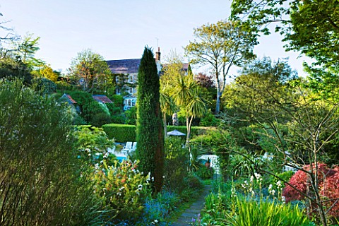 MILLE_FLEURS__GUERNSEY_VIEW_ACROSS_THE_SWIMMING_POOL_TO_THE_HOUSE_WITH_LIBERTIA_GRANDIFLORA_IN_THE_F