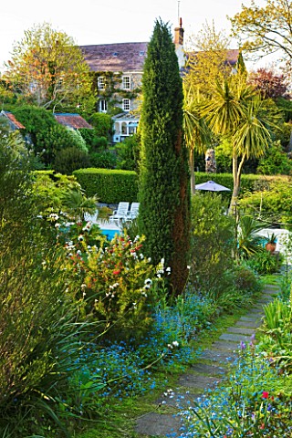 MILLE_FLEURS__GUERNSEY_VIEW_ALONG_PATH_TO_SWIMMING_POOL_AND_HOUSE_BEYOND_WITH_LIBERTIA_GRANDIFLORA