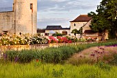 CHATEAU DU RIVAU  LOIRE VALLEY  FRANCE: THE CHATEAU IN THE EVENING WITH SESLERIA AUTUMNALIS  ALLIUM GIGANTEUM AND STIPA TENUIFOLIA