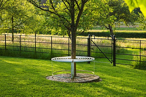 GIPSY_HOUSE__BUCKINGHAMSHIRE_METAL_TREE_SEAT_ON_LAWN_WITH_THE_MEADOW_BEHIND