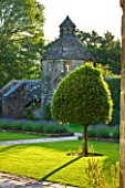 NYMANS  SUSSEX. THE NATIONAL TRUST: THE FORECOURT IN EVENING LIGHT WITH STONE PATHS  DOVECOTE AND STANDARD BAY TREE  JUNE  EVENING LIGHT
