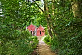 PAINSWICK ROCOCO GARDEN  GLOUCESTERSHIRE: THE RED HOUSE SEEN ALONG A WOODLAND PATH
