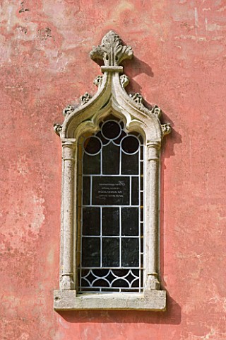 PAINSWICK_ROCOCO_GARDEN__GLOUCESTERSHIRE_WINDOW_DETAIL_ON_THE_RED_HOUSE_SEEN_ALONG_A_WOODLAND_PATH