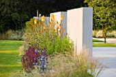 DEW POND HOUSE: DESIGN BY WILSON MCWILLIAM STUDIO - SANDSTONE PATIO WITH RENDERED WALL  LAWN  KNIPHOFIA TAWNY KING  ERYNGIUMS BLUE STAR AND BLAUKAPPE   SALVIA CARADONNA