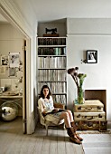 TWIG HUTCHINSON HOUSE  LONDON: TWIG IN WHITE LIVING ROOM WITH CHAIR  BOOKCASE  ALLIUMS IN GLASS JAR WITH SUITCASES BENEATH