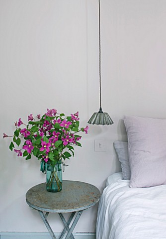 TWIG_HUTCHINSON_HOUSE__LONDON_BEDROOM_WITH_BED__BEDSIDE_LIGHT_AND_SMALL_TABLE_WITH_PINK_CLEMATIS_IN_