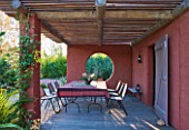 AFRICAN GARDEN  PROVENCE  FRANCE: DESIGNER DOMINIQUE LAFOURCADE: TERRACOTTA-TONED STUCCO WALLS AND DINING AREA WITH TABLE AND CHAIRS