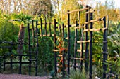 AFRICAN GARDEN  PROVENCE  FRANCE: DESIGNER DOMINIQUE LAFOURCADE: BLACK WOODEN STAKE FENCE PLANTED WITH PYRACANTHA