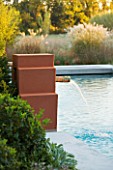 AFRICAN GARDEN  PROVENCE  FRANCE: DESIGNER DOMINIQUE LAFOURCADE: TERRACOTTA COLOURED WATER FOUNTAINS SPURT INTO THE SWIMMING POOL WITH PAMPAS GRASS BEHIND