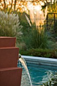 AFRICAN GARDEN  PROVENCE  FRANCE: DESIGNER DOMINIQUE LAFOURCADE: TERRACOTTA COLOURED WATER FOUNTAINS SPURT INTO THE SWIMMING POOL WITH PAMPAS GRASS BEHIND. EVENING LIGHT