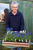 RICHARD HOBBS GARDEN  NORFOLK: RICHARD WITH MUSCARI IN FRONT OF GREEN SHED