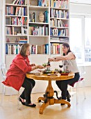 SHELLEY VON STRUNCKEL APARTMENT  LONDON: SHELLEY EATING AT WOODEN CIRCULAR TABLE AND PHILIPPE STARCK CHAIRS  WITH BOOKSHELF BEHIND