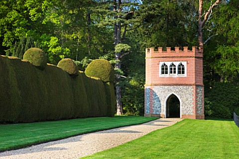 DODDINGTON_PLACE_GARDENS__KENT_MASSIVE_CLIPPED_YEW_HEDGES_IN_SPRING__GRAVEL_PATH_AND_FLINT_AND_BRICK