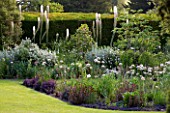 GLYNDEBOURNE, EAST SUSSEX: VIEW THROUGH YEW TREES TO LAWN AND BORDER WITH EREMURUS, ALLIUMS AND BERBERIS - HERBACEOUS, SUMMER