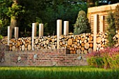 GARDEN IN KENT DESIGNED BY BELLA WHITELEY: LOG WALL BEHIND BRICK WALL. RECYCLING, RECYCLED, FENCE, FENCING, WOODEN, LOGS, BOUNDARY, BOUNDARIES