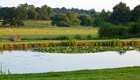 BROUGHTON_CASTLE_OXFORDSHIRE_VIEW_OUT_ACROSS_THE_LAKE_TO_COUNTRYSIDE_BEYOND__SUMMER_COUNTRY_GARDEN_R