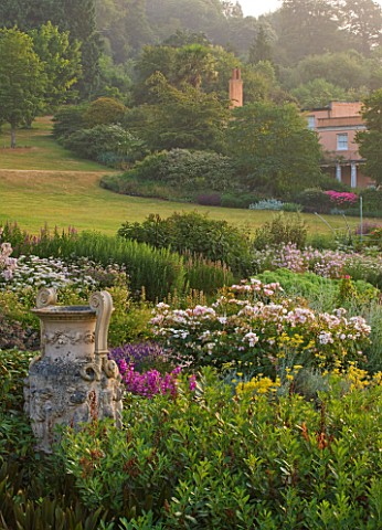 KILLERTON__DEVON_THE_NATIONAL_TRUST__THE_HERBACEOUS_BORDER_WITH_COADE_STONE_URN_AND_WEST_FRONT_OF_TH