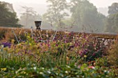 KILLERTON  DEVON: THE NATIONAL TRUST - THE HERBACEOUS BORDER WITH DIERAMA AND URN WITH PARKLAND BEYOND