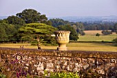 KILLERTON  DEVON: THE NATIONAL TRUST- HERBACEOUS GARDEN - URN ON TOP OF WALL WITH PARKLAND BEYOND - EVENING LIGHT
