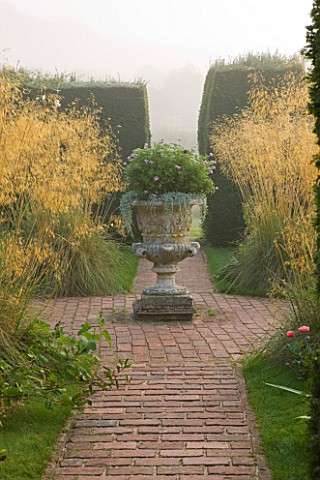 GLYNDEBOURNE_EAST_SUSSEX_BRICK_PATH_TO_STONE_URN_AT_CENTRE_OF_FORMAL_GARDEN_WITH_STIPA_GIGANTEA__MIS