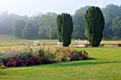 GLYNDEBOURNE, EAST SUSSEX: THE MAIN LAWN WITH BENCHES AND YEWS, BORDER WITH SEDUMS AND GAURA LINDHEIMERI - SHEEP BEYOND IN FIELD, COUNTRY GARDEN